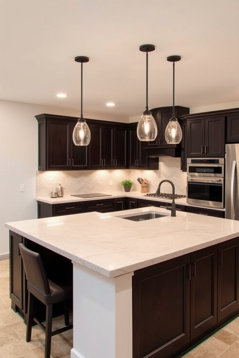 A stylish basement kitchen featuring a tile backsplash that adds visual interest. The cabinetry is a rich navy blue with brass hardware, and the countertops are a sleek white quartz. In the center, a large island provides ample workspace and seating with modern bar stools. Soft pendant lights hang above the island, illuminating the space and creating a warm ambiance.