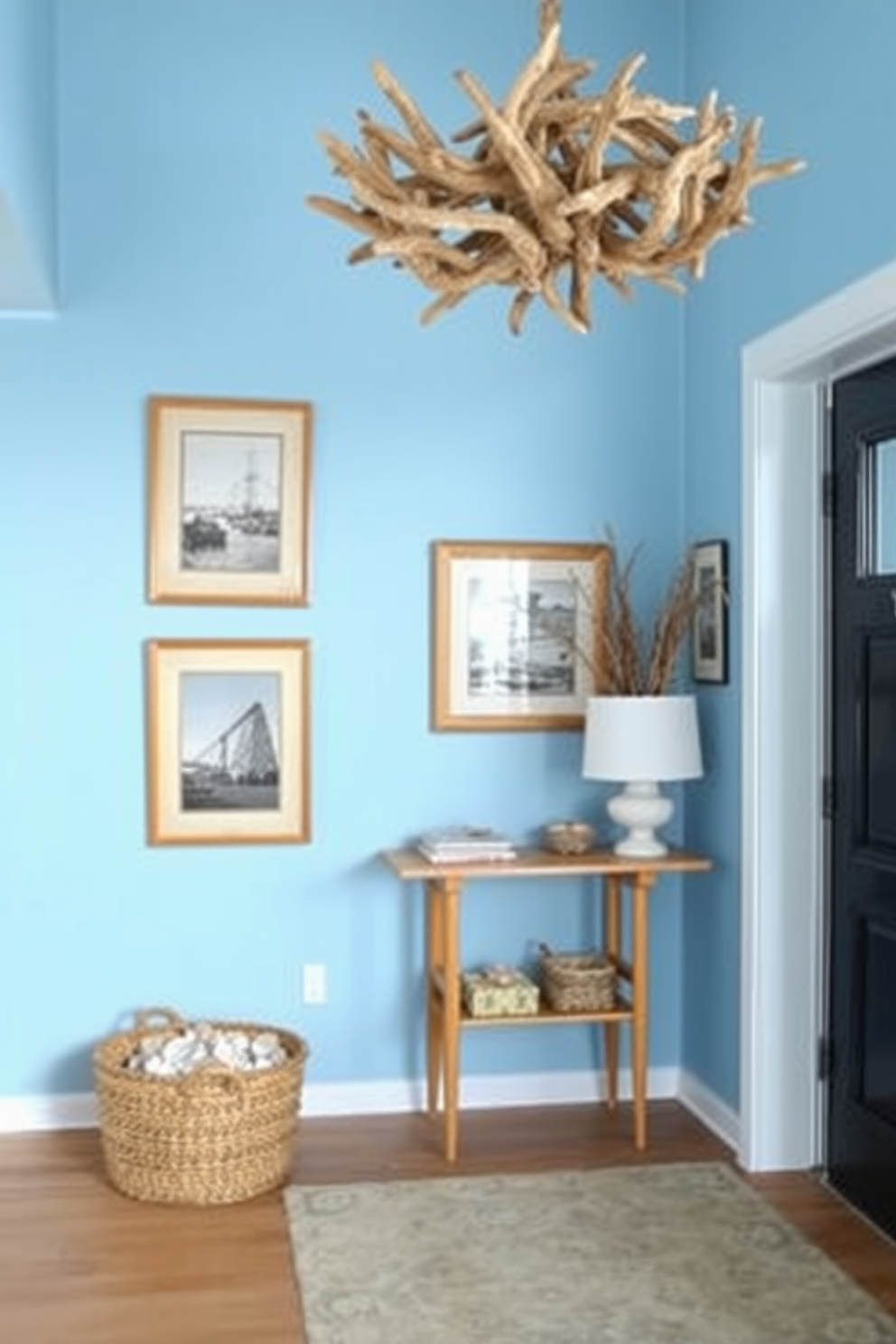 Coastal blue hues create a serene and inviting atmosphere in the foyer. The walls are painted in a soft blue shade, while natural wood accents are incorporated through a console table and framed artwork. Decorative elements include a large woven basket filled with seashells and a coastal-themed rug that adds texture. A statement light fixture made of driftwood hangs from the ceiling, enhancing the beachy vibe of the space.