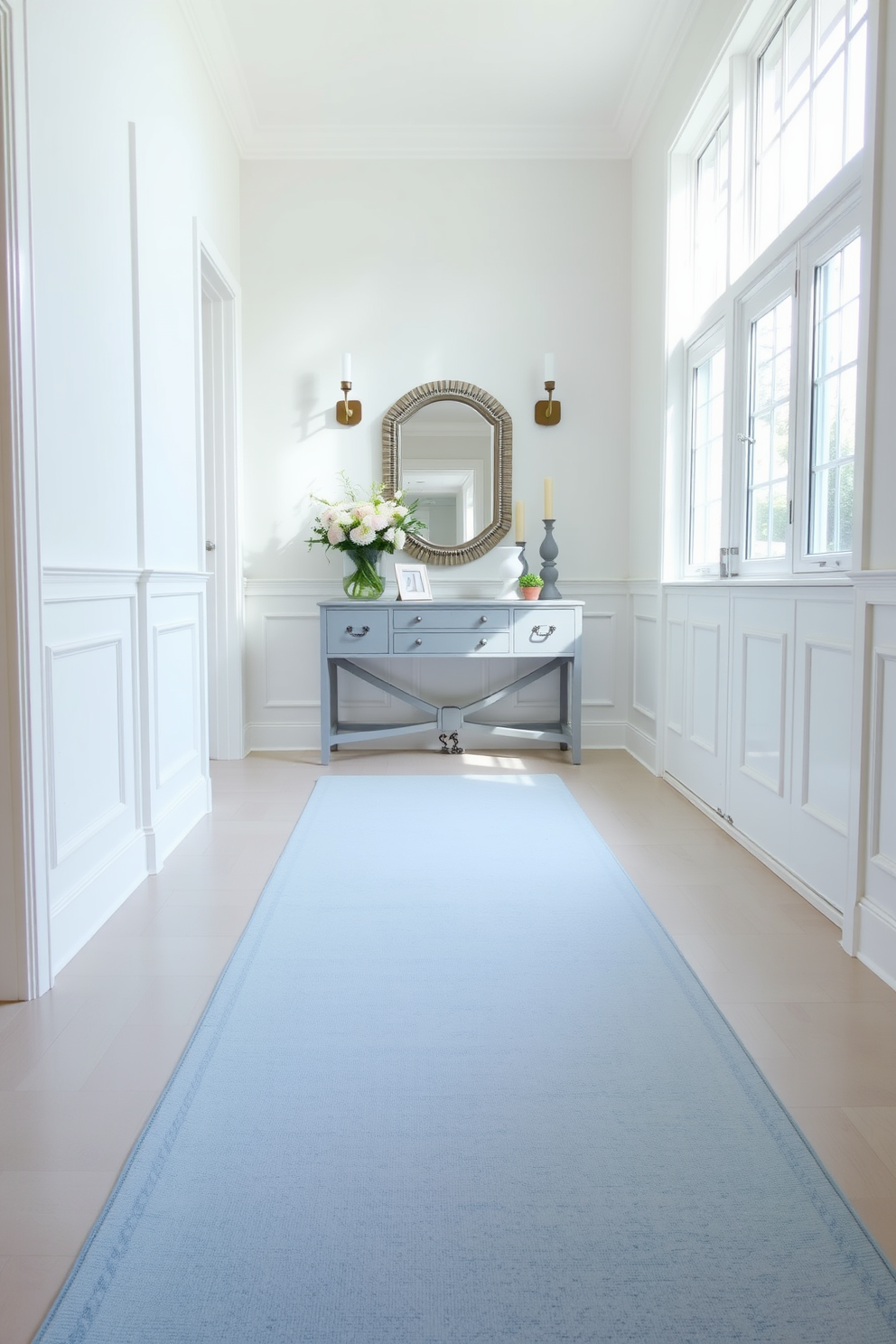 A soft pastel blue runner rug extends elegantly across the foyer, creating a serene and inviting atmosphere. The walls are adorned with light-colored wainscoting, and a statement console table sits against one side, topped with decorative items and a fresh bouquet of flowers. Natural light pours in through a large window, illuminating the space and enhancing the calming color palette. A pair of stylish wall sconces flank a mirror above the console, adding both functionality and a touch of sophistication to the design.
