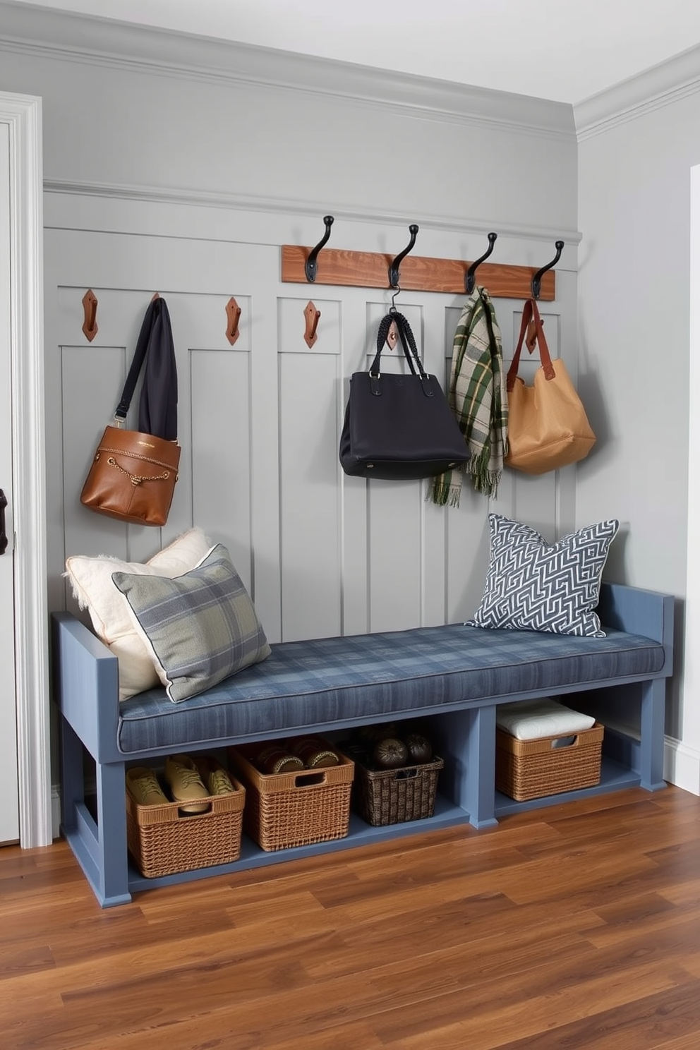 A stylish mudroom featuring a denim blue bench adorned with plush cushions. The walls are painted in a soft gray, complemented by rustic wooden hooks for hanging coats and bags.