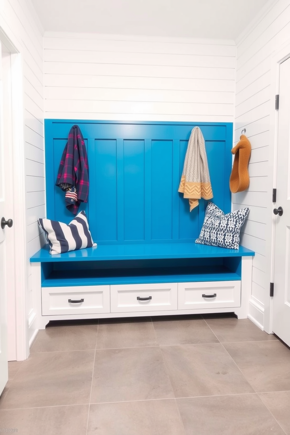 A cerulean blue built-in bench with storage is the focal point of this mudroom, providing a stylish and functional seating area. The walls are adorned with shiplap paneling painted in a crisp white, while the floor features a durable gray tile that complements the vibrant bench.
