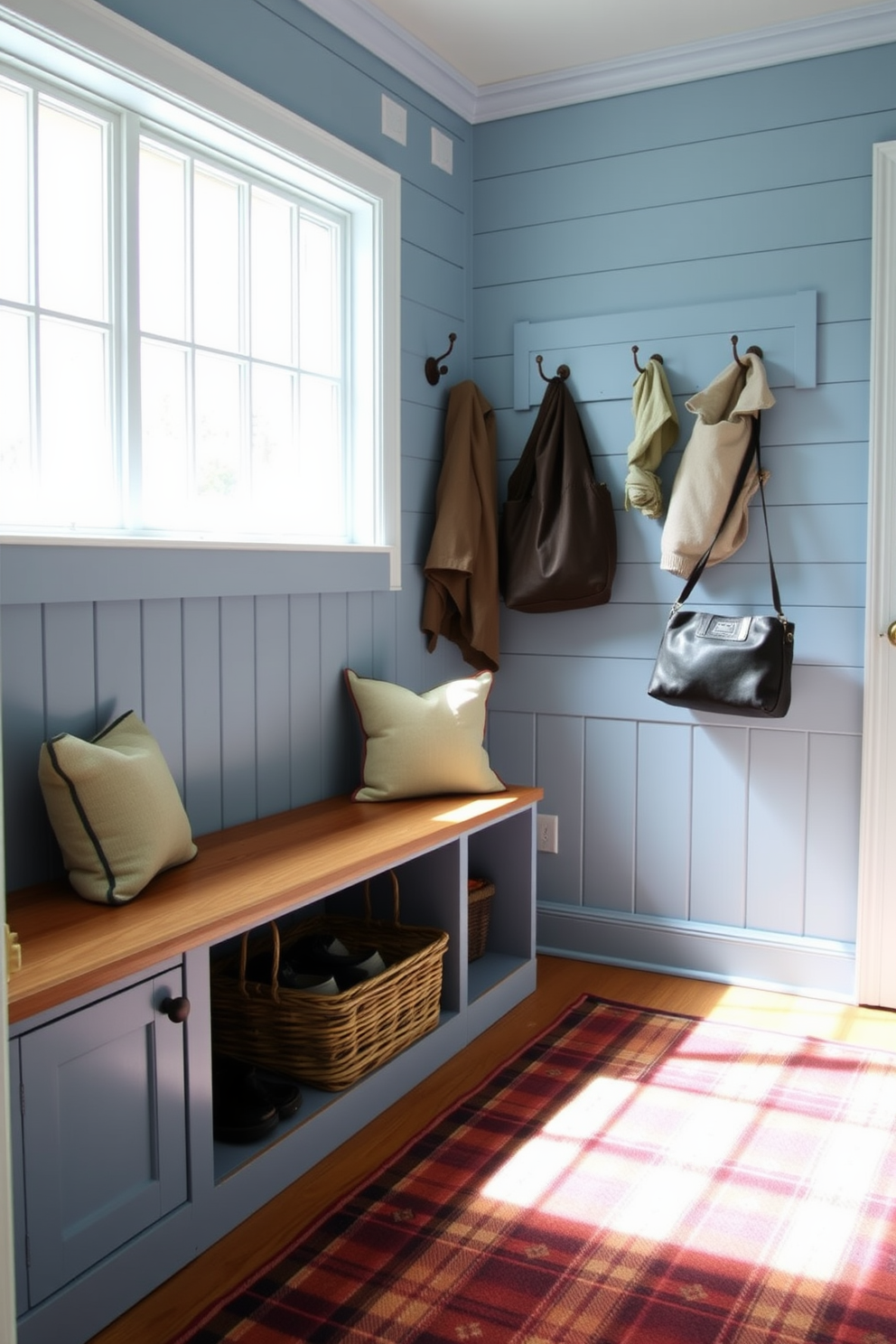 A periwinkle blue mudroom exuding rustic charm features a wooden bench with built-in storage underneath. The walls are adorned with shiplap, and a collection of vintage hooks line the entryway for hanging coats and bags. Natural light floods the space through a large window, illuminating a woven basket filled with shoes. A cozy area rug with a plaid pattern adds warmth and texture to the floor.