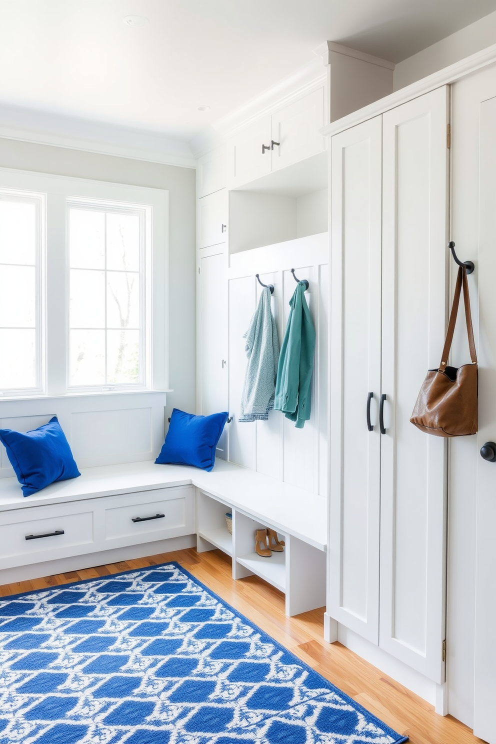 A minimalist mudroom featuring royal blue accents. The space includes a sleek bench with royal blue cushions and built-in storage cabinets painted in a soft white. The walls are adorned with simple hooks for hanging coats, while a patterned rug in shades of blue and white adds a touch of warmth. Large windows allow natural light to flood the area, enhancing the clean and airy feel of the design.