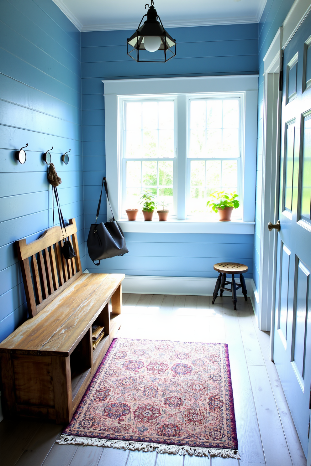 Faded blue shiplap lines the walls of a charming mudroom, creating a warm and inviting atmosphere. The space features a rustic wooden bench with storage underneath, paired with vintage hooks for hanging coats and bags. Natural light floods in through a large window, illuminating a patterned area rug that adds a pop of color to the floor. Potted plants sit on the windowsill, enhancing the vintage appeal and bringing a touch of nature indoors.