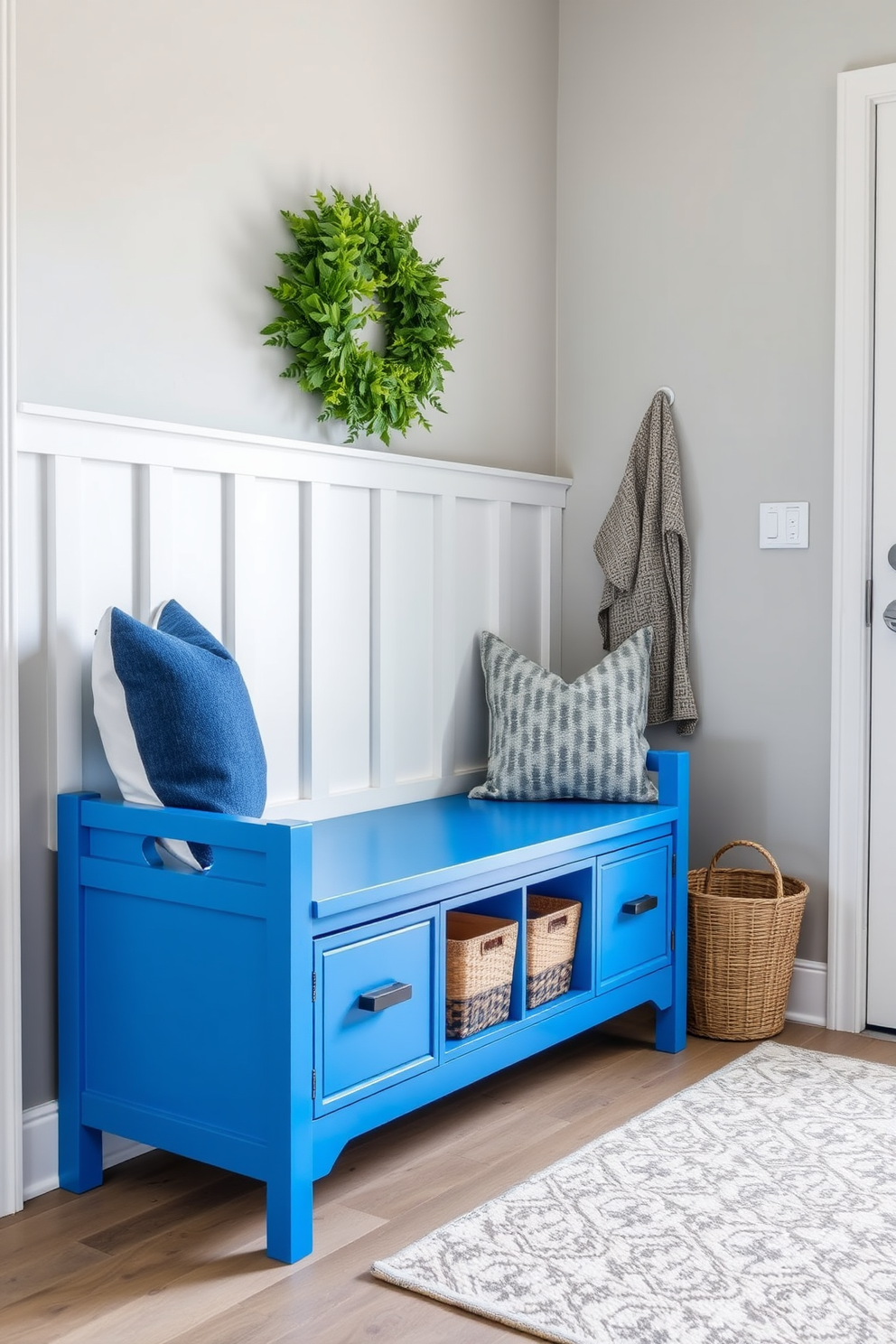 A bright blue accent bench with drawers sits in a stylish mudroom, providing both functionality and a pop of color. The walls are painted in a soft gray, complementing the vibrant bench and creating a welcoming entryway.
