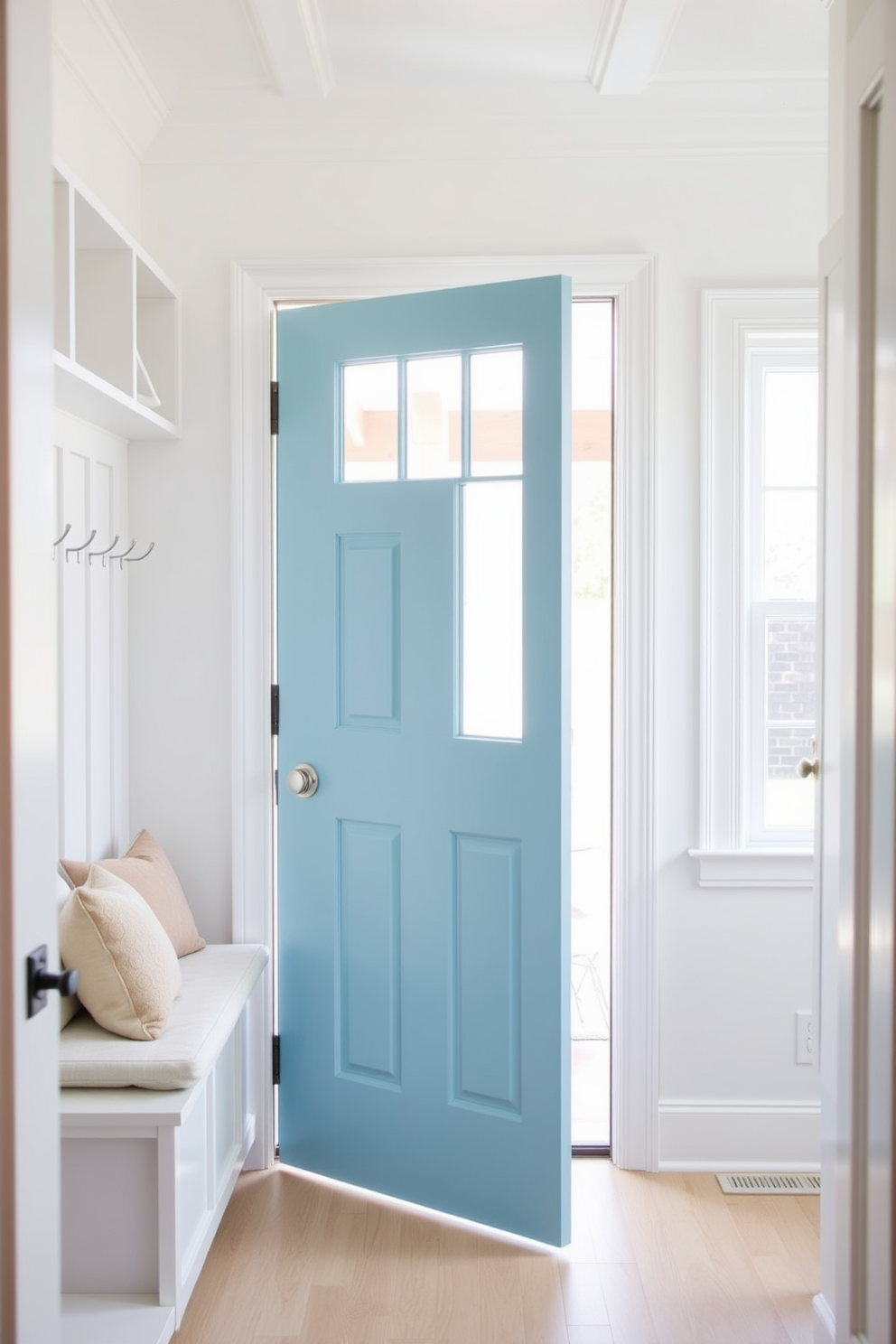 A sky blue mudroom door with a glass panel welcomes you into a bright and airy space. The walls are painted in a soft white, complementing the light wood flooring and creating a fresh, inviting atmosphere. To the left of the door, there is a built-in bench with plush cushions, providing a cozy spot to sit. Hooks line the wall above the bench, offering a practical solution for hanging coats and bags.