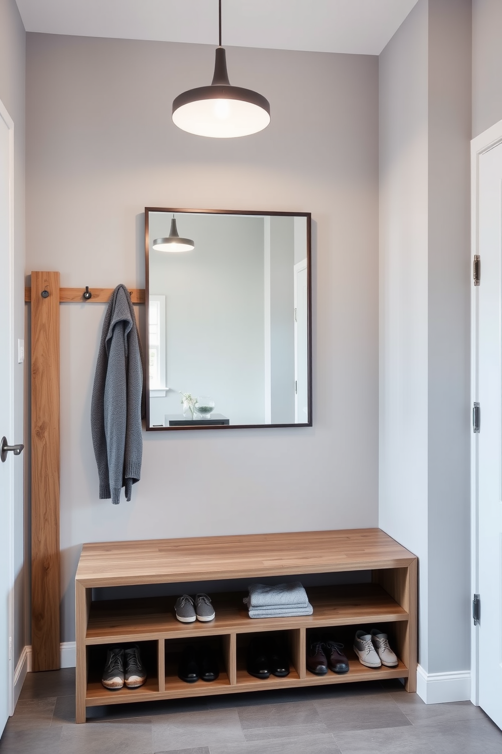 A sleek shoe storage solution designed for an entrance foyer features a minimalist wooden bench with built-in cubbies for shoes underneath. The walls are adorned with a soft gray paint, and a stylish coat rack is mounted beside the entrance for added functionality. The foyer is illuminated by a modern pendant light that hangs gracefully from the ceiling. A large mirror with a slim frame reflects the space, making it feel open and inviting while adding a touch of elegance.
