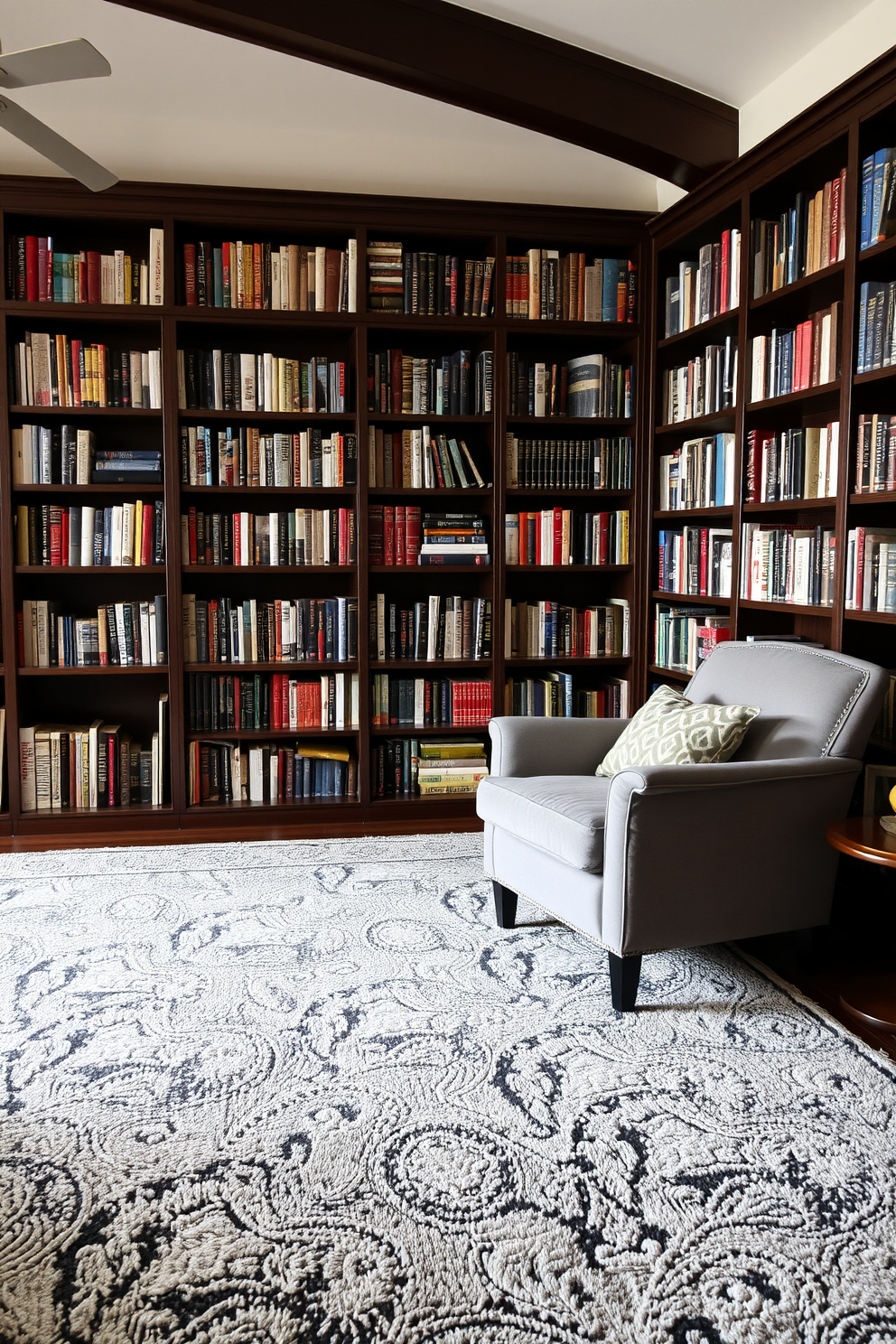 A cozy home library featuring layered gray rugs that create a warm and inviting atmosphere. The walls are lined with dark wood bookshelves filled with an array of books, and a plush gray armchair sits in the corner, perfect for reading.