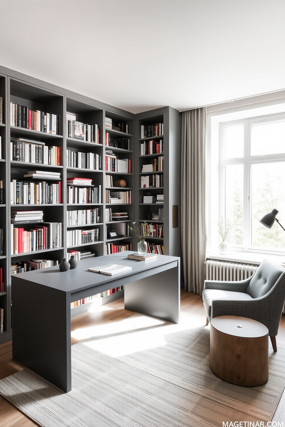 A sleek gray desk is positioned against a wall lined with bookshelves filled with an array of books and decorative objects. Soft natural light filters in through a large window, illuminating the space and highlighting the minimalist decor. The library features a cozy reading nook with a comfortable armchair in a complementary gray tone. A subtle area rug anchors the space, adding warmth while maintaining the overall modern aesthetic.