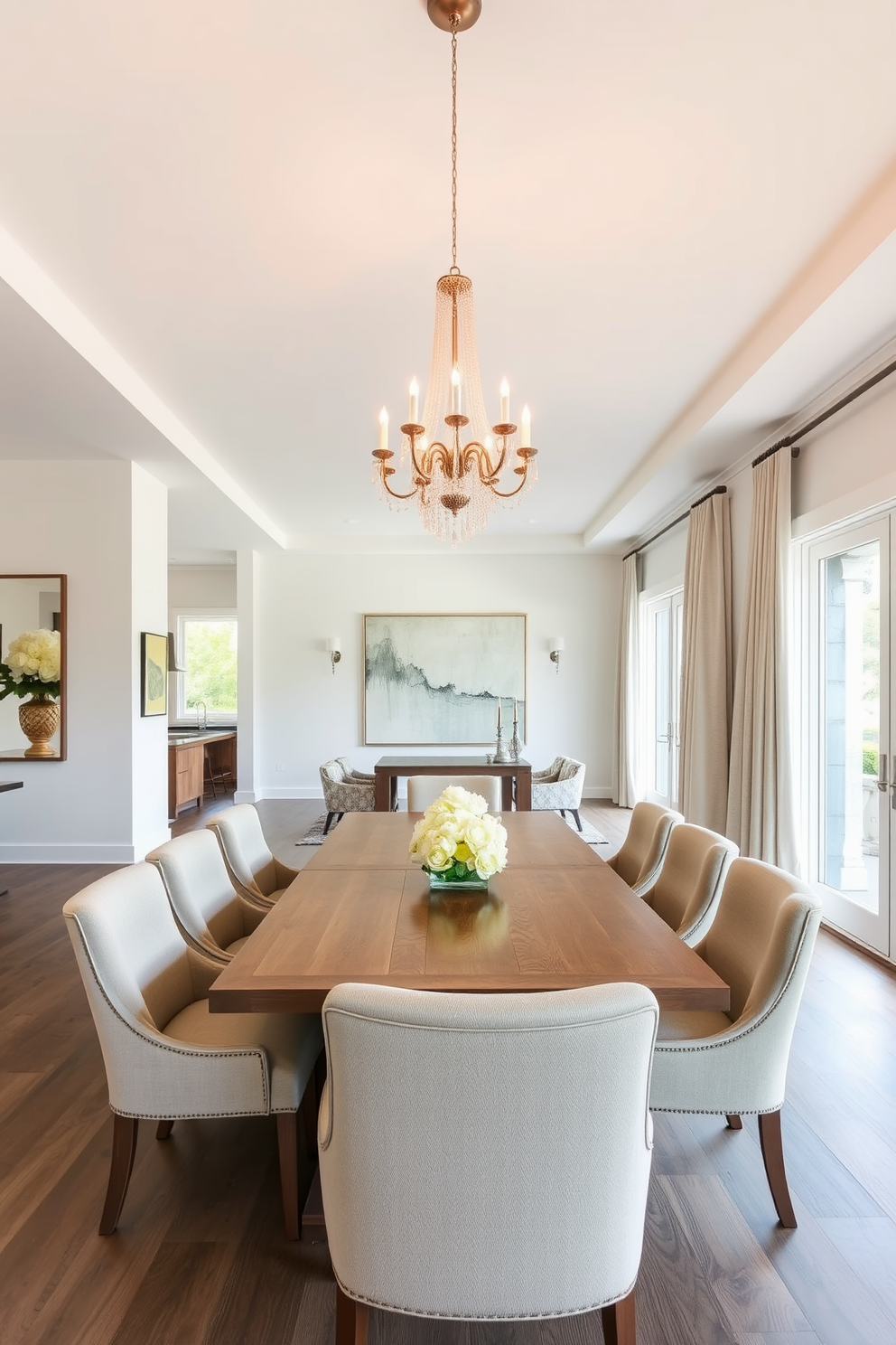 Open concept dining area with a large wooden table that seats eight. The table is surrounded by upholstered chairs in a neutral fabric, and a stunning chandelier hangs above, providing warm light. The walls are painted in soft white, creating an airy feel, while a large piece of abstract art adds a pop of color. Large windows allow natural light to flood the space, complemented by elegant drapes in a light fabric.
