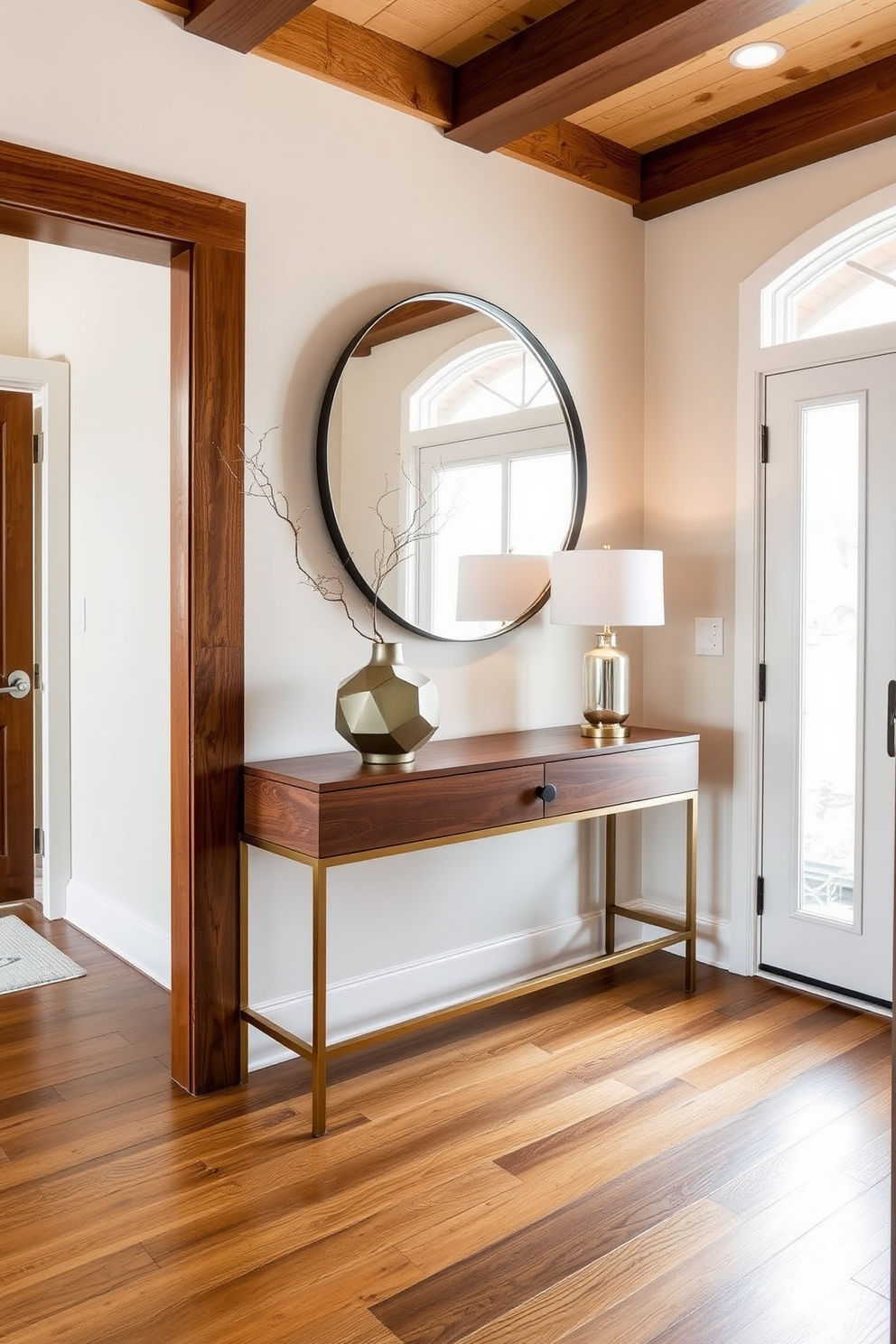 A welcoming foyer features a striking combination of warm wood and sleek metal elements. A wooden console table with a brushed brass base sits against the wall, adorned with a geometric vase and a stylish lamp. The walls are painted in a soft cream color, complementing the rich tones of the wooden flooring. A large round mirror with a metal frame hangs above the console, reflecting natural light from a nearby window.