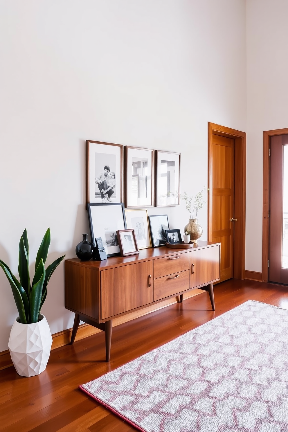 A stylish foyer features a sleek console table adorned with framed family photos that add a personal touch. The walls are painted in a soft neutral tone, complemented by warm wooden accents and a geometric area rug that enhances the Mid Century Modern aesthetic.