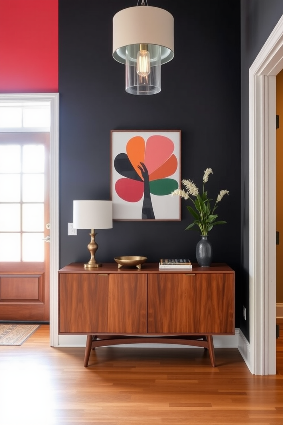 A striking foyer features a bold colored accent wall adorned with vibrant artwork that captures attention. The space is illuminated by a stylish pendant light, enhancing the Mid Century Modern aesthetic with clean lines and organic shapes. A sleek console table in a rich wood finish stands against the wall, complemented by a decorative bowl and a small potted plant. The flooring is a warm hardwood, creating a welcoming atmosphere that invites guests into the home.