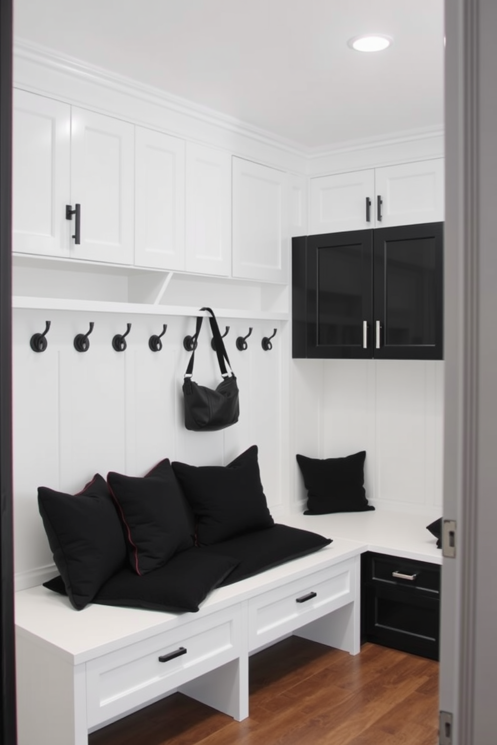 Crisp black and white color scheme. The mudroom features sleek black cabinetry with white accents, providing a striking contrast. A large white bench with black cushions offers a comfortable seating area. Above the bench, a series of black hooks are mounted on the wall for hanging coats and bags.