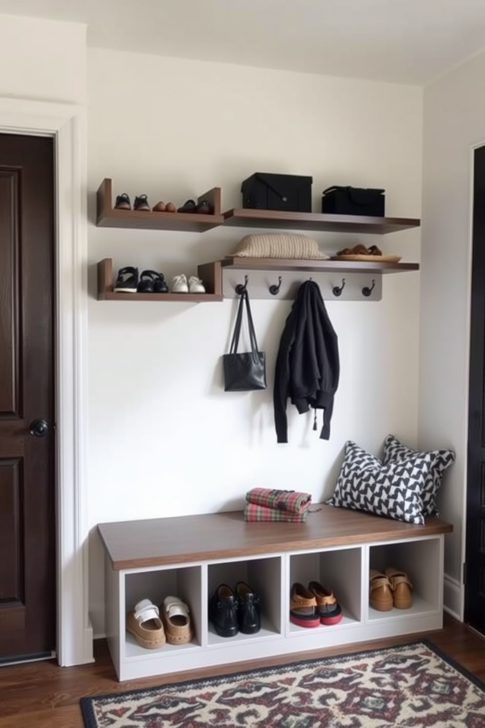 Sleek floating shelves are mounted on the wall, providing stylish storage for shoes and accessories. The mudroom features a combination of durable materials, including a bench with storage underneath and hooks for coats. The walls are painted in a light neutral color, creating a bright and airy atmosphere. A patterned rug adds a touch of warmth and comfort to the space, complementing the overall modern design.
