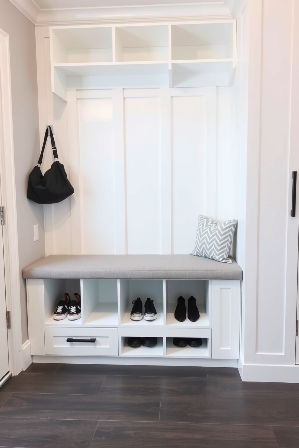A modern mudroom featuring a built-in bench with side shoe cubbies. The bench is upholstered in a soft gray fabric, providing comfort and style while the cubbies are designed with a sleek white finish for a clean look.