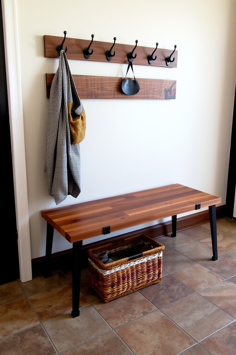 A reclaimed wood bench with metal accents is placed against the wall, showcasing a rustic yet modern aesthetic. The bench features a sturdy design with a weathered finish, complemented by sleek metal legs that add an industrial touch. Above the bench, a series of hooks are mounted on the wall, providing ample space for coats and bags. The floor is adorned with durable tiles that can withstand heavy foot traffic, while a woven basket sits beneath the bench for storing shoes.