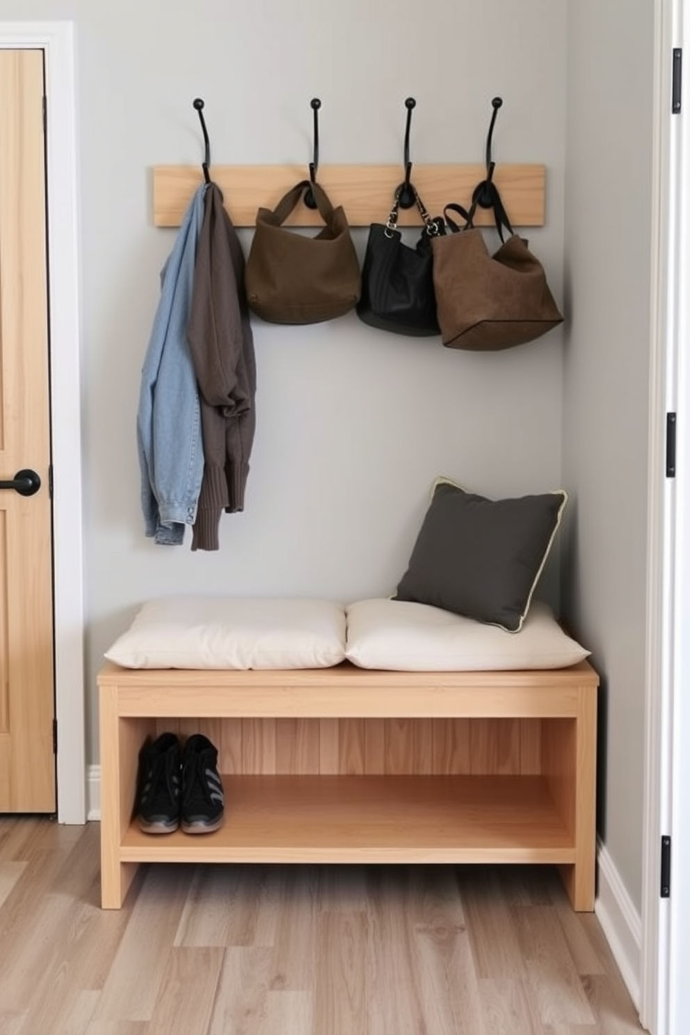 A narrow bench designed for small spaces features a sleek, minimalist style with a light wood finish. It is placed against a wall, complemented by hooks above for hanging coats and bags, creating an organized and inviting mudroom area. The bench includes built-in storage underneath for shoes and outdoor gear, maximizing functionality without sacrificing aesthetics. Soft cushions on top provide comfort while maintaining a clean and modern look in the entryway.