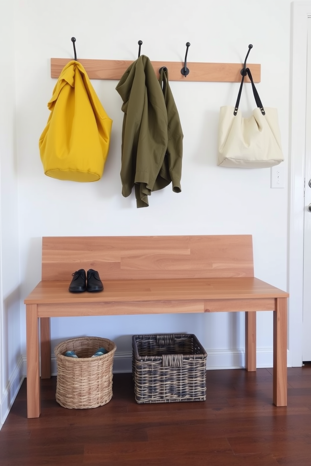 A simple bench with a natural finish is placed against a wall in the mudroom. The bench features clean lines and a minimalist design, providing a functional yet stylish seating area for removing shoes. Above the bench, hooks are mounted for hanging coats and bags, creating an organized space. A woven basket sits underneath the bench, offering storage for shoes and outdoor gear.