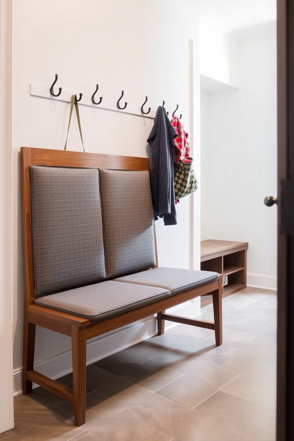 A mudroom features a bench with a stylish backrest design that combines functionality and aesthetics. The bench is upholstered in a durable fabric, with a sleek wooden frame that complements the overall decor of the space. On the wall above the bench, there are hooks for hanging coats and bags, adding to the practicality of the mudroom. The floor is finished with a weather-resistant tile that adds a touch of elegance while being easy to clean.
