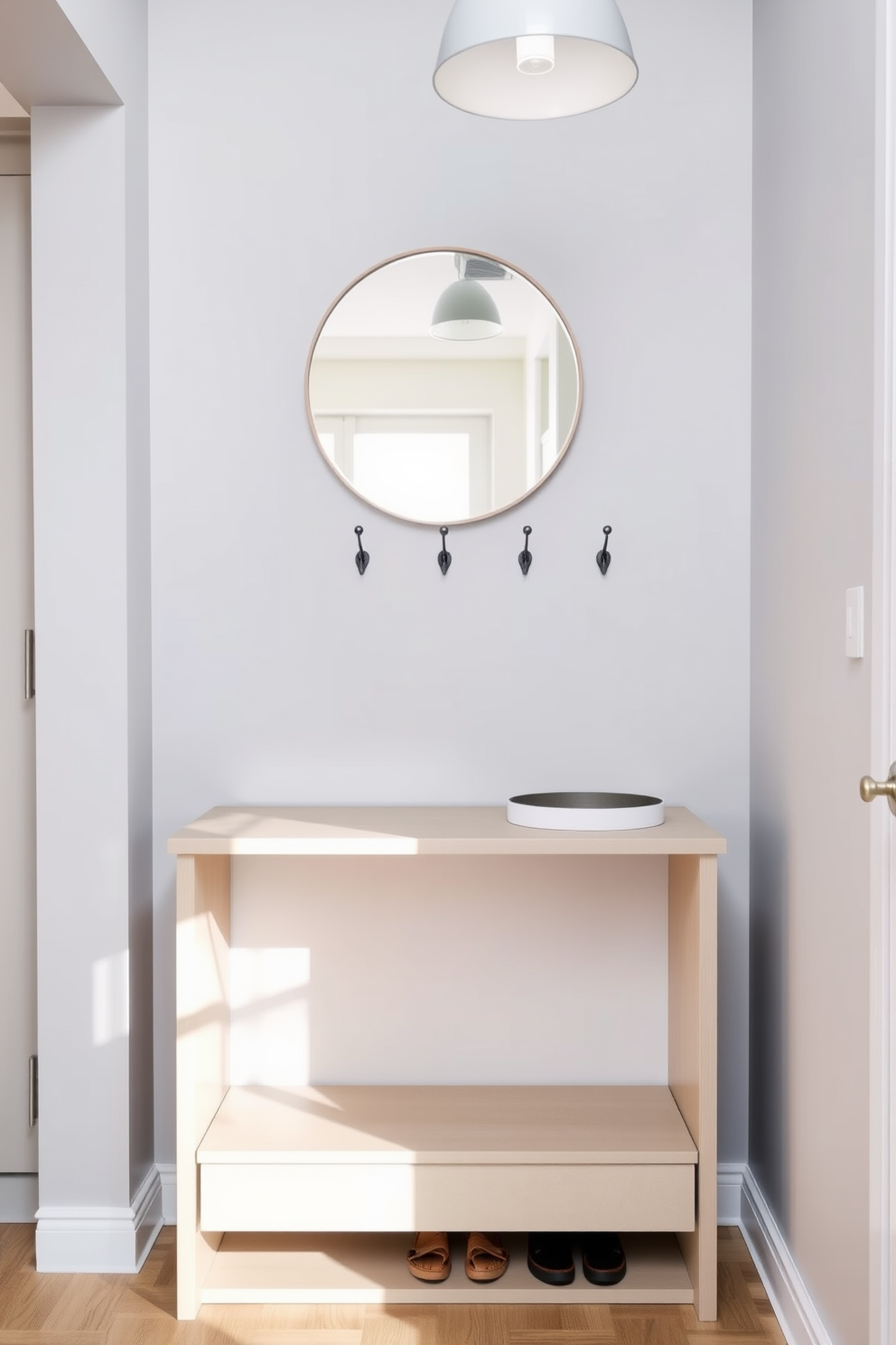 A minimalist entryway features a sleek console table against a light gray wall. Above the table, a simple round mirror reflects natural light, while a row of elegant hooks provides a functional touch. The narrow apartment design incorporates a compact shoe storage unit beneath the console, maximizing space. Soft lighting from a pendant lamp creates a warm and inviting atmosphere.