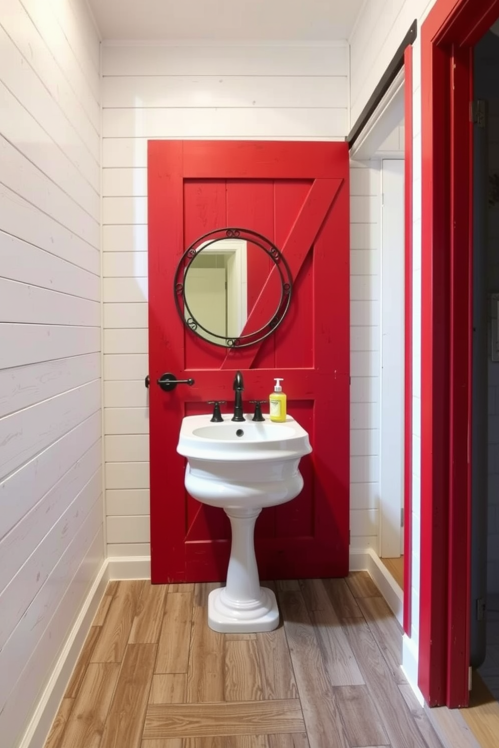 A rustic red barn door serves as the entrance to a charming powder room. Inside, the walls are adorned with shiplap paneling, and a vintage pedestal sink adds a touch of elegance. The flooring features distressed wood planks that complement the barn door's color. A round mirror with a wrought iron frame hangs above the sink, enhancing the rustic aesthetic.