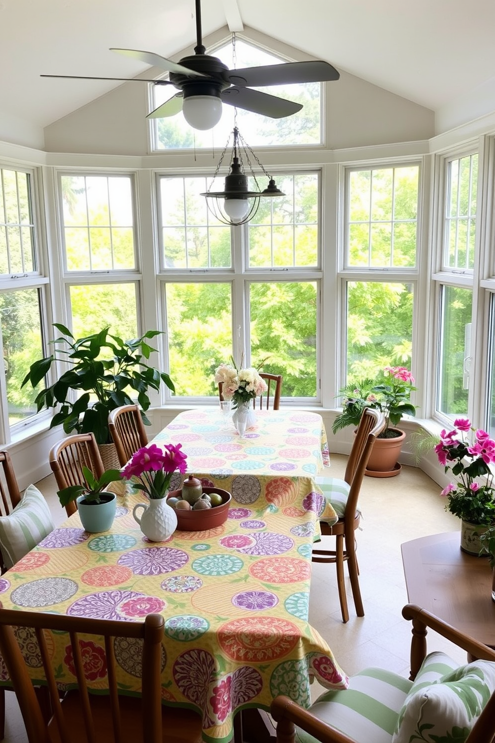 A bright and inviting sunroom filled with natural light. The dining table is adorned with vibrant patterned tablecloths that add a cheerful touch to the space. Surrounding the table are comfortable chairs with soft cushions in coordinating colors. Large windows showcase lush greenery outside, while potted plants and flowers add life to the room.